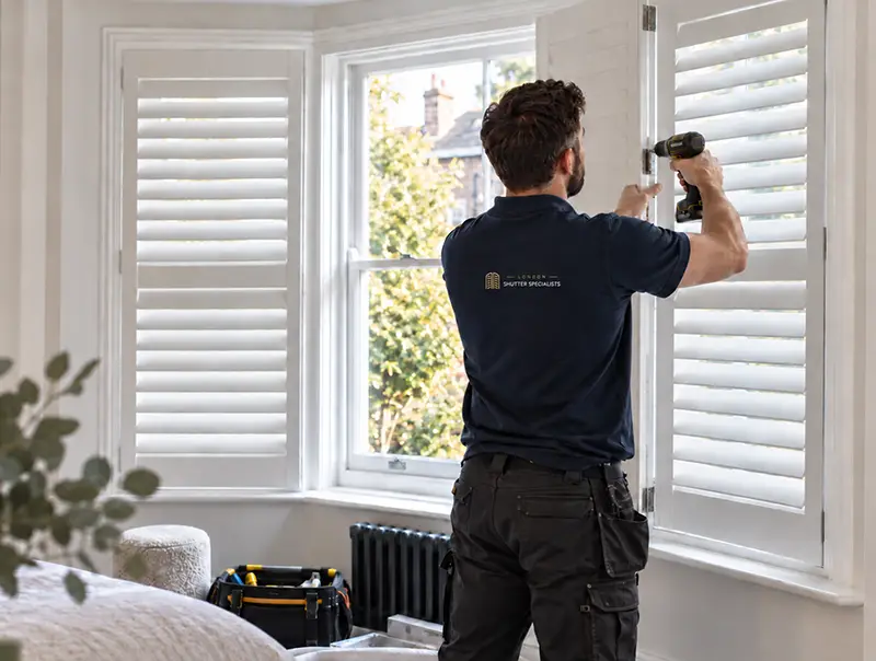 London Shutter Specialists installer securing white shutters to a bay window